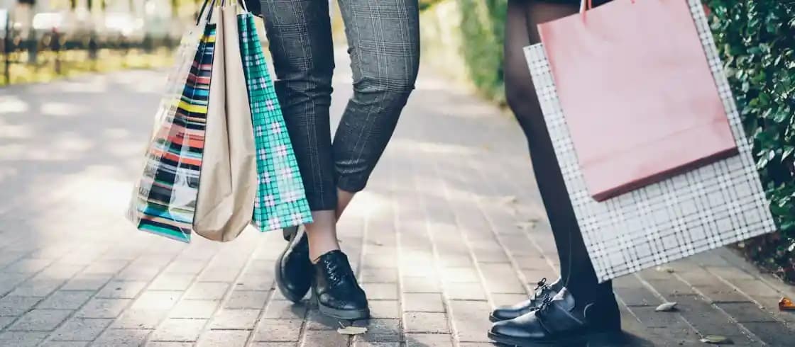 Hai người đứng trên vỉa hè, tay cầm túi mua sắm